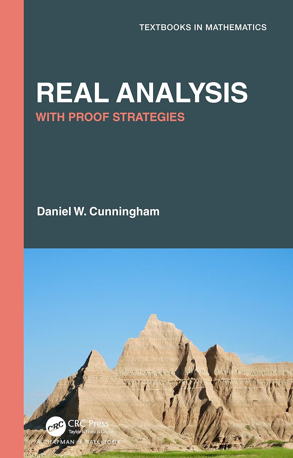 Book cover of "Real Analysis with Proof Strategies" by Daniel W. Cunningham, part of the Textbooks in Mathematics series. The top half features a dark teal background with bold white and coral-colored text, while the bottom half shows a scenic photograph of rocky, mountainous terrain under a clear blue sky. Published by CRC Press, a Chapman & Hall Book.